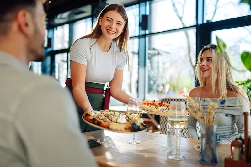 Young female server delivering food to a couple in a restaurant.
