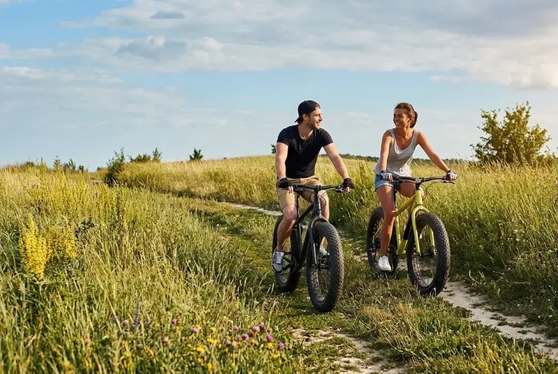 Man and woman riding a bike in a field of grass.