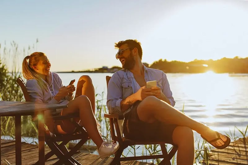 Couple sitting on a dock next to a lake.