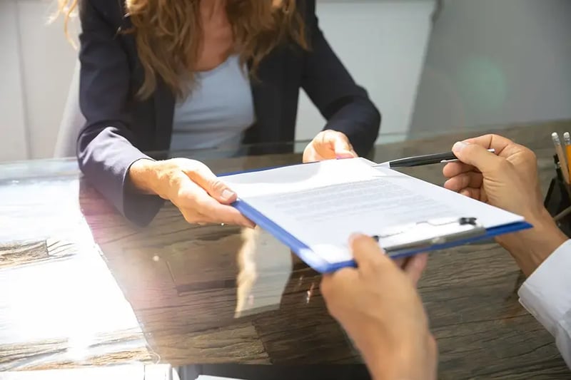 Woman handing paperwork to another person.