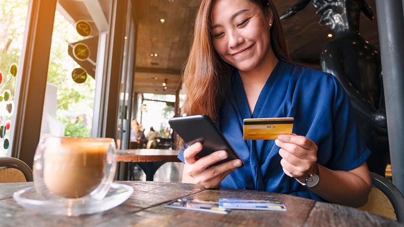 Woman in a coffee shop holding cell phone and credit card.