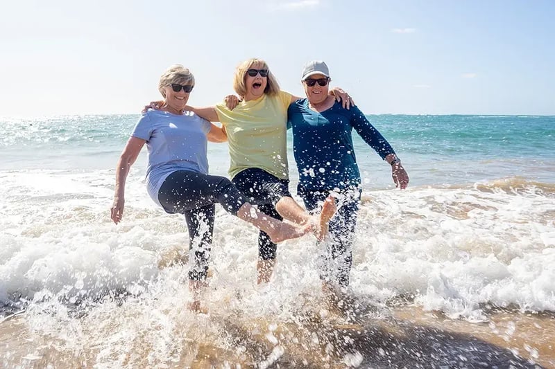 Three women kicking their feet in the surf.