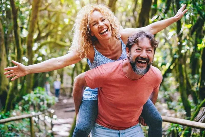 Woman riding piggyback on a man in the forest.