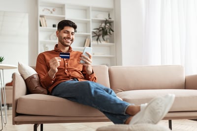 Man sitting on sofa with a cell phone and credit card.