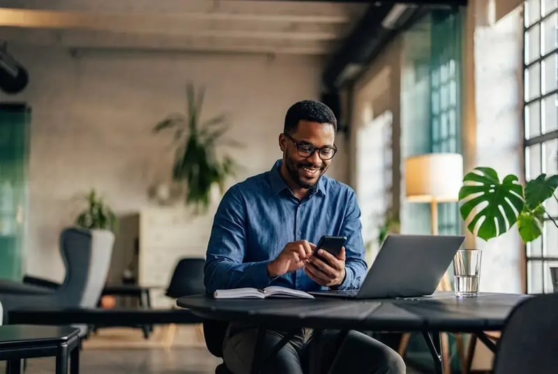 Man at a desk with a laptop computer and cell phone.