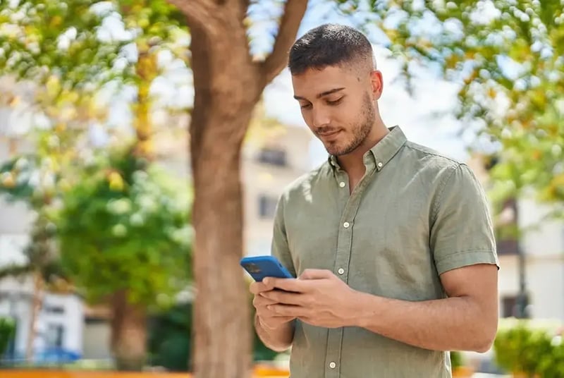 Man near a tree looking at a cell phone.