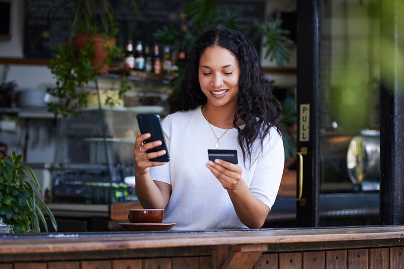 Woman with a cell phone looking at a credit card.