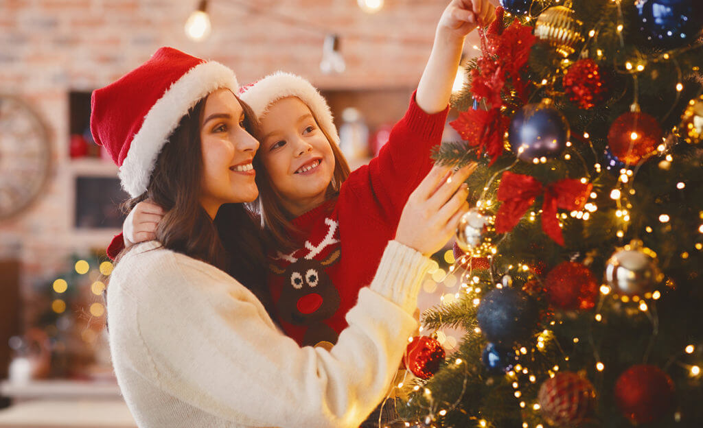 Festive mother and daughter decorating Christmas tree at home