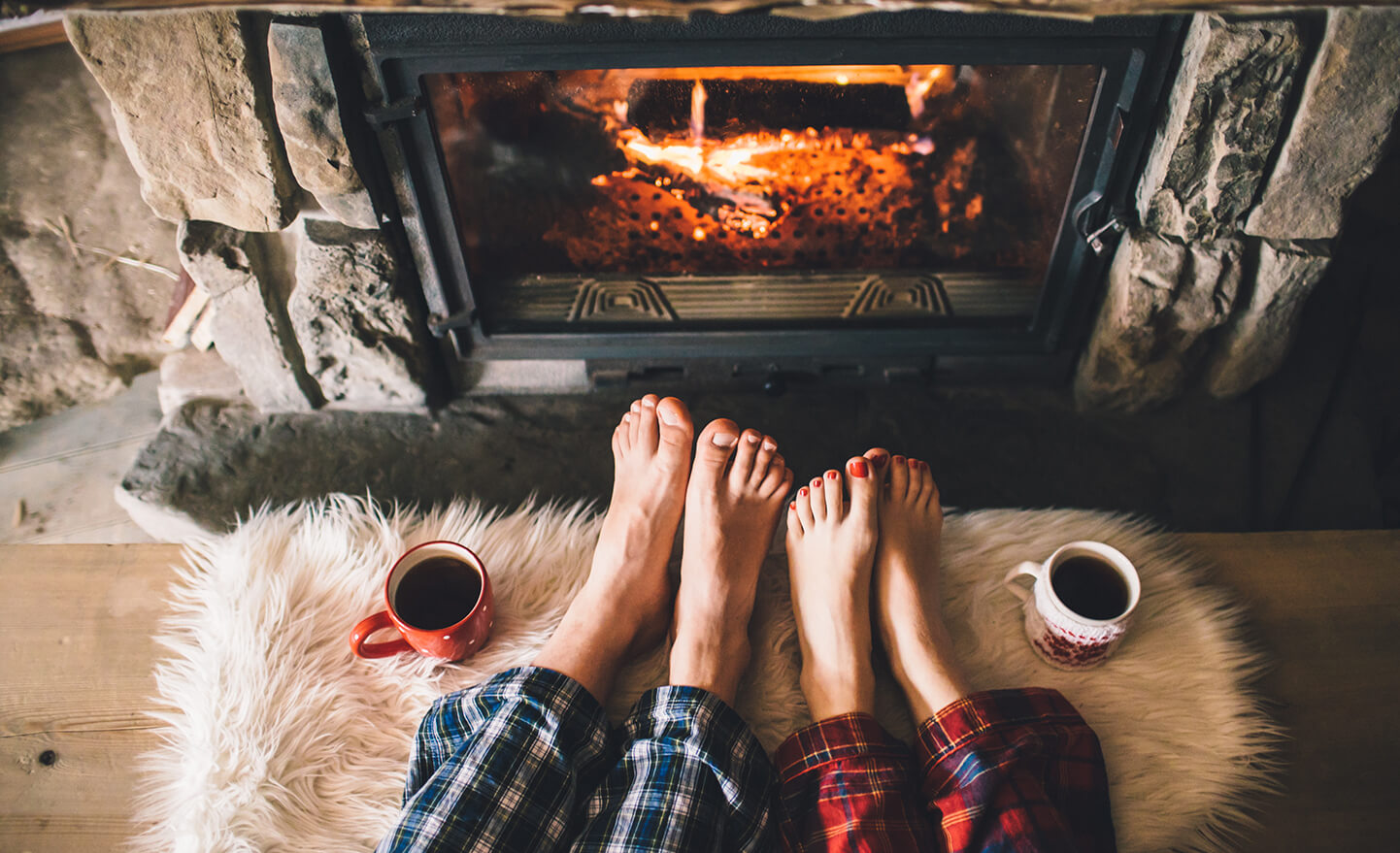 Bare couple feet by the cozy fireplace. Man and Woman relaxes by warm fire with a cup of hot drink and warming up her feet. Close up on feet. Winter and Christmas holidays concept