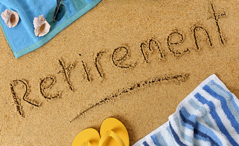 Close-up of word 'retirement' written in sand with beach towels and slippers surrounding