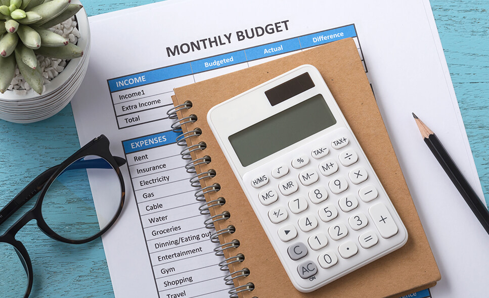 Closeup photo of a monthly budget printout, a notebook, calculator and glasses on a desk