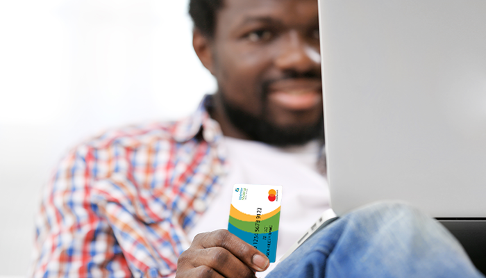 Person sitting with their laptop holding their Keesler Federal Credit Union debit card.