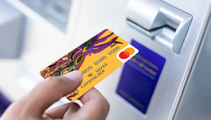 A hand placing a Mardi Gras themed Keesler debit card into an ATM machine.