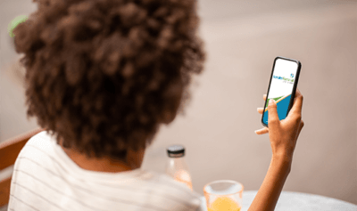 Back of a person's head holding a mobile phone while sitting by a table.