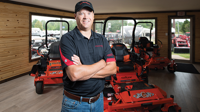 A smiling person inside a room with their arms crossed with red racing cars in the background