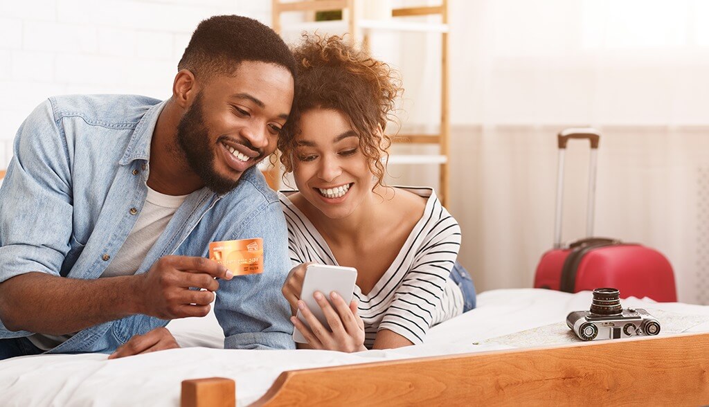 Couple laying on bed using credit card on their phone