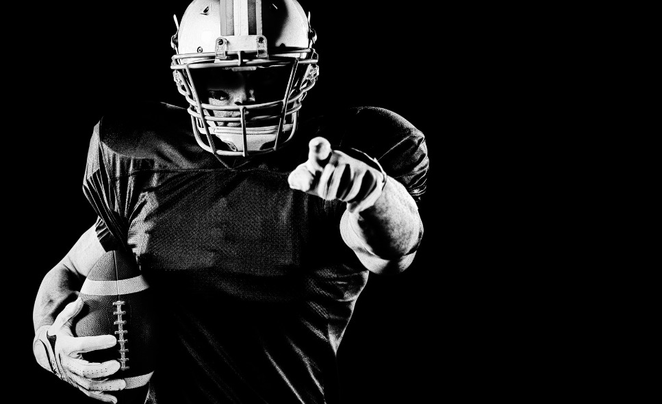 black and white photo of football player holding football and pointing at screen