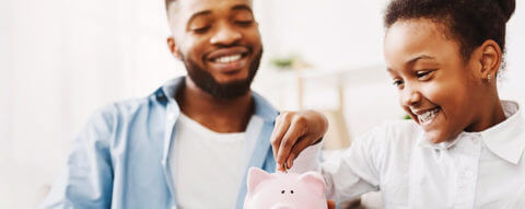 Photo of a parent watching their child put a coin in the piggy bank