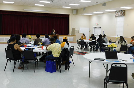 Image of conference room with people sitting around tables listening to speaker on podium