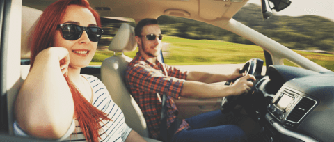 Couple with sunglasses inside a car driving speedily down the road