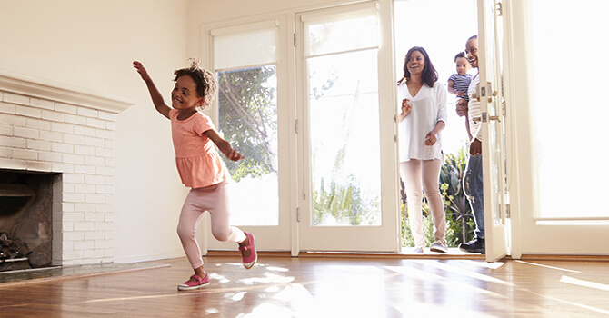 A child playing in the living room of their family's new home as their parents and siblings walk in behind them.