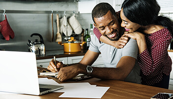 Couple hugging each other in the kitchen in front of laptop