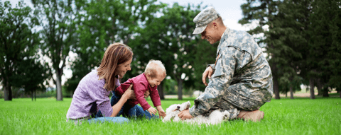 Photo of military family playing in a field with dog